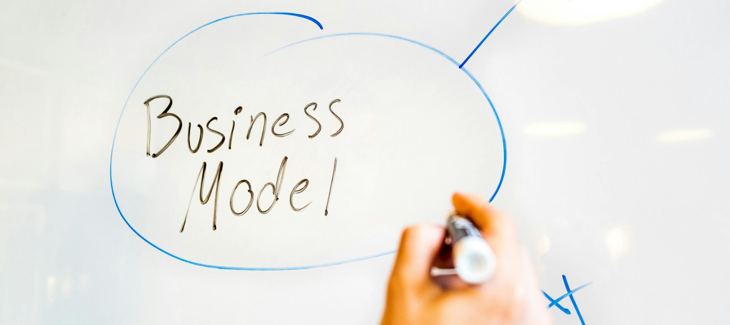 A person plans their business model by writing on a whiteboard.
